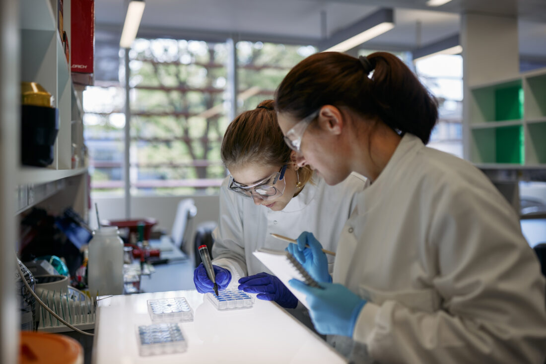 Two scientists discuss an experiment while looking over a bottom lit panel